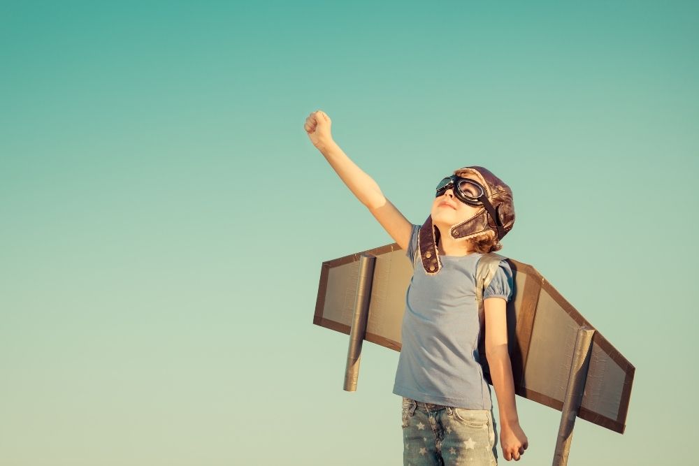 criança vestida como aviador com braços levantados.
