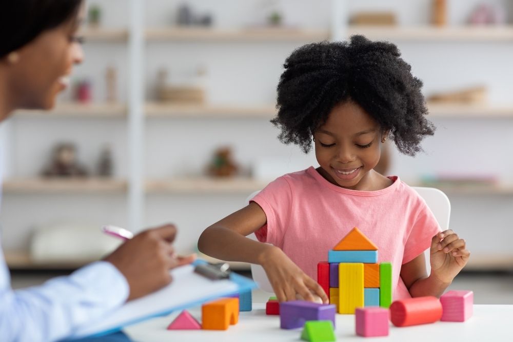 criança brincando com blocos coloridos sob a supervisão de um adulto.