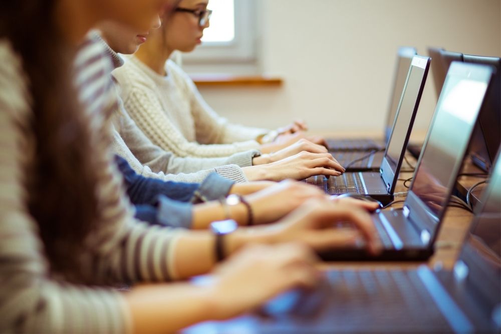 pessoas digitam em notebooks em sala de aula.